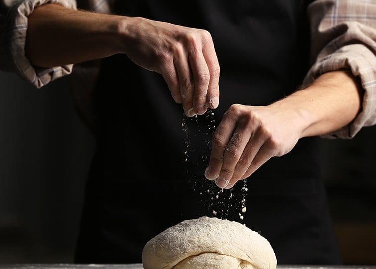 GCA baker sprinkling flour over kneaded dough