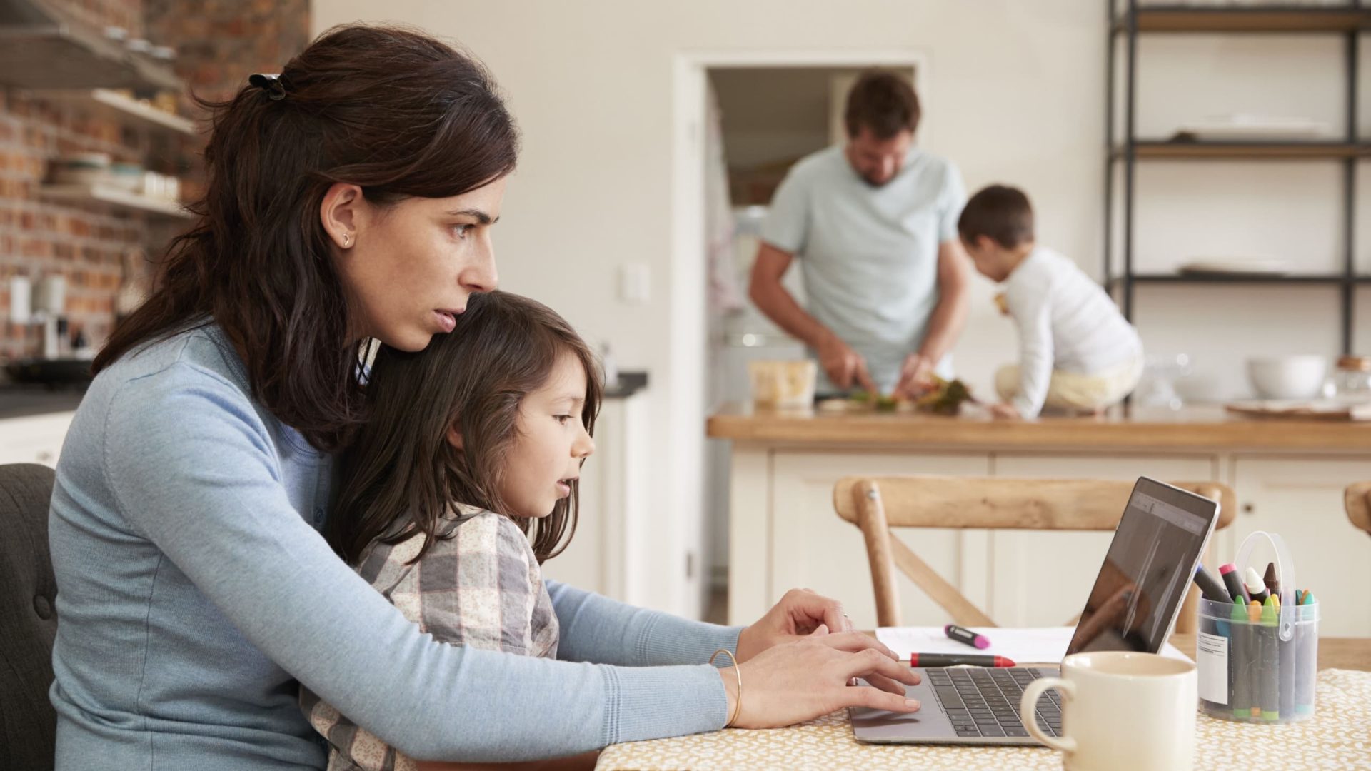 Busy Family Home With Mother Working As Father Prepares Meal