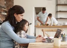 Busy Family Home With Mother Working As Father Prepares Meal