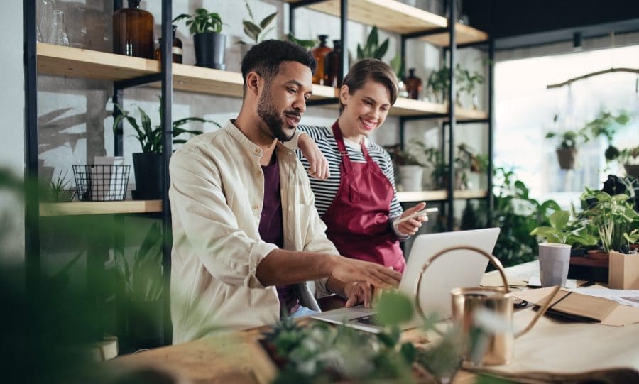 Shop assistants with laptop working in potted plant store, small business concept.