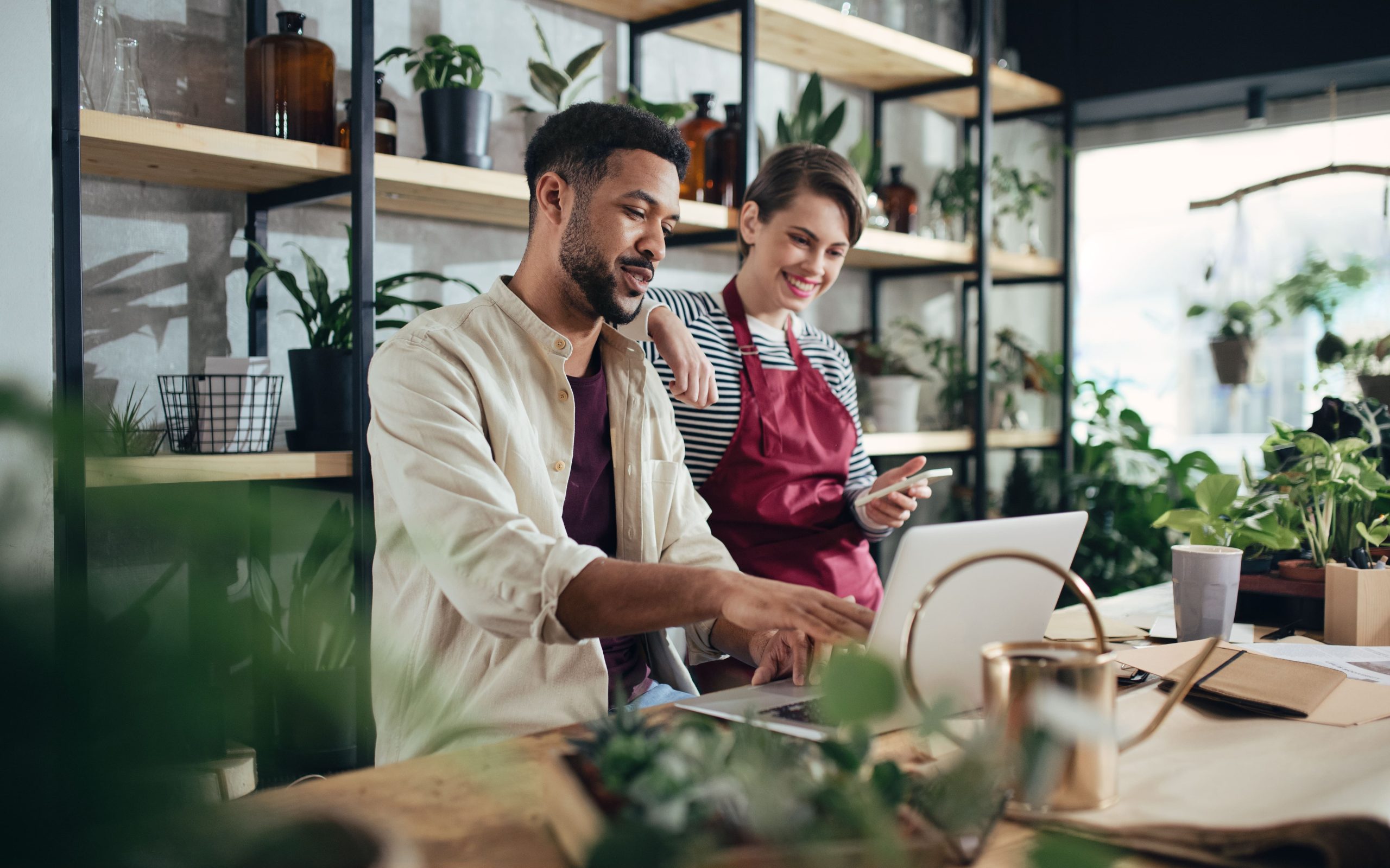 Shop assistants with laptop working in potted plant store, small business concept.