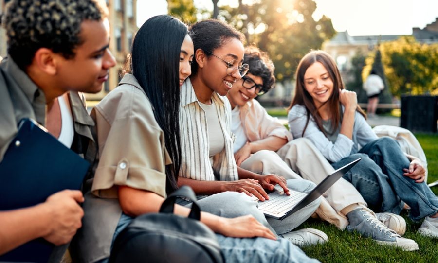 students sitting on lawn with laptop